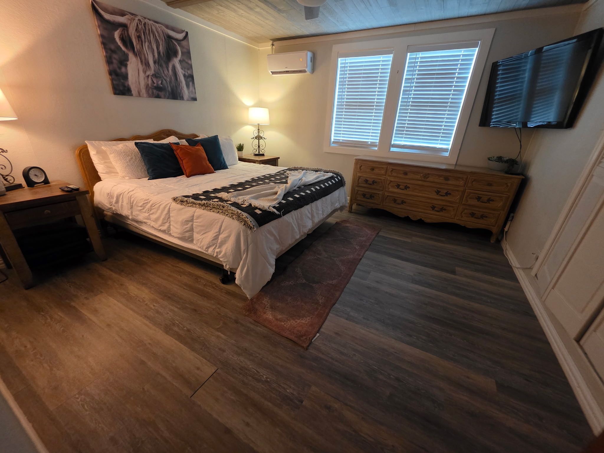 Un dormitorio con cama, mesitas de noche, cómoda, alfombra y televisor montado.
