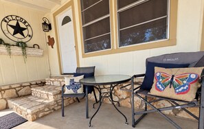 A patio with stone steps, a round table, two chairs with cushions, a welcome sign, and a butterfly pillow.