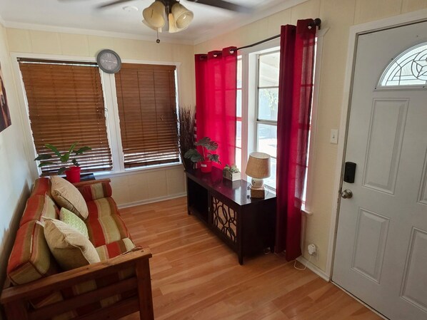 A room with a wooden floor, a sofa, a table with a lamp, a potted plant, and a door with a window.