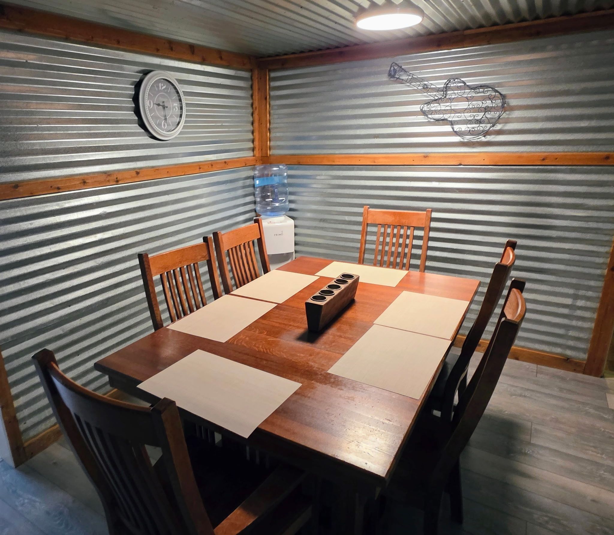 Un comedor con una mesa y sillas de madera, un dispensador de agua y un reloj en la pared.