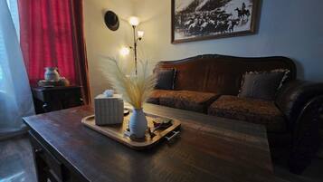 Una sala acogedora con una mesa de centro de madera, un florero con plantas secas, una lámpara y un sofá con cojines estampados.