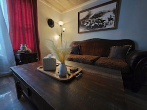 A cozy living room with a wooden coffee table, a vase with dried plants, a lamp, and a sofa with patterned cushions.