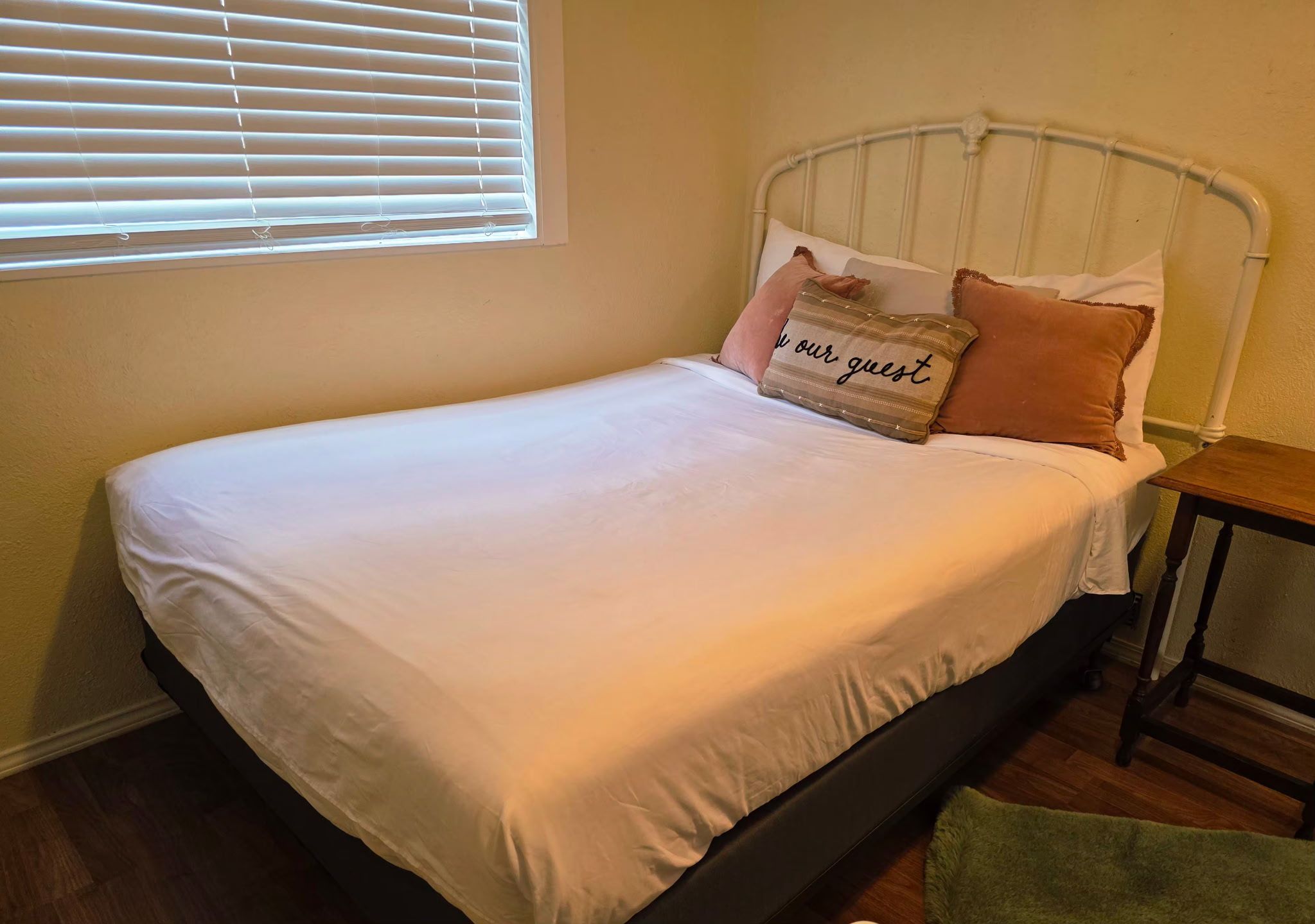 Un lit avec un matelas blanc, une tête de lit en métal et deux oreillers, dont l’un porte un message.