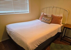 A bed with a white mattress, a metal headboard, and two pillows, one with a message.