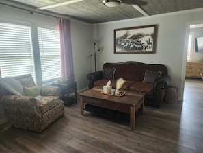 Ein Wohnzimmer mit Sofa, Sessel, Couchtisch und einem Gemälde an der Wand.