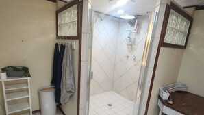 Une salle de bain avec une douche, un lavabo, une petite table et une étagère.