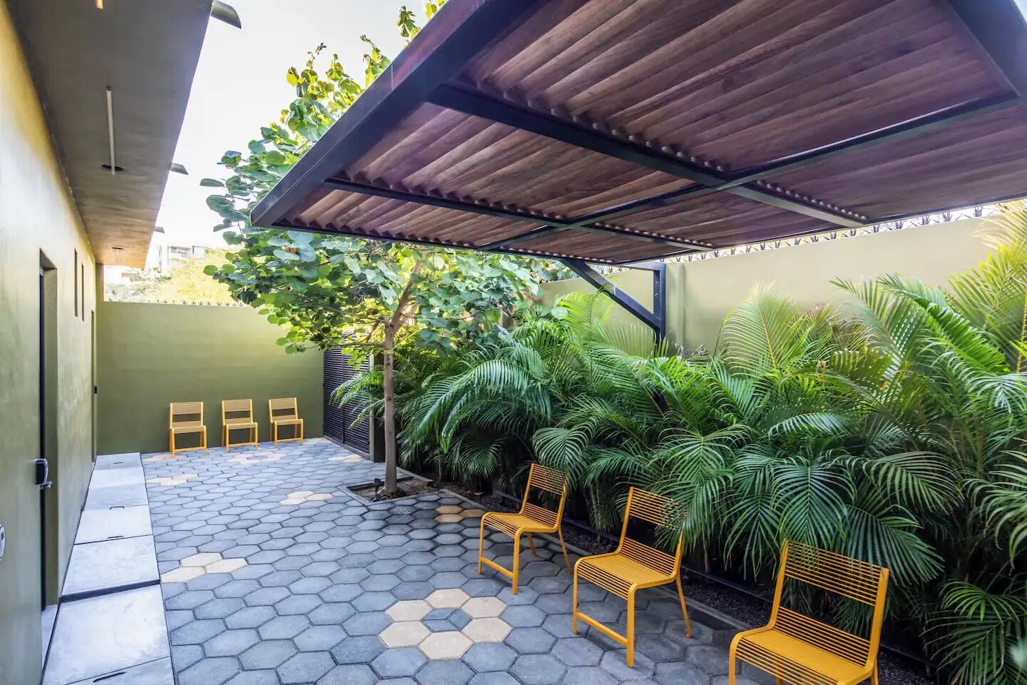 A covered patio area with hexagonal tiles, wooden chairs, and lush green plants.