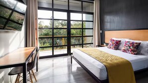A modern hotel room with a large window, a bed with colorful pillows, a desk, and a chair. - A&R Luxury Suite (San José del Cabo)