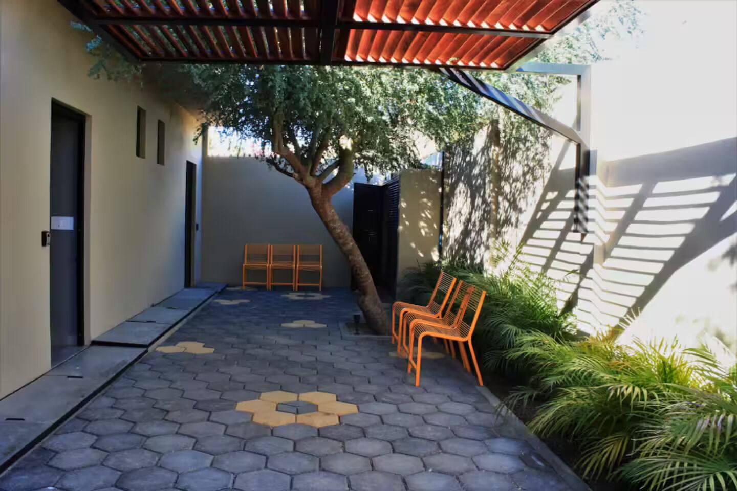 A covered outdoor area with hexagonal tile flooring, a tree, and orange chairs.