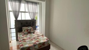 A bedroom with a bed, a window with curtains, a chair, and a door leading to another room.