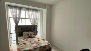 A bedroom with a bed, a window with curtains, a chair, and a door.