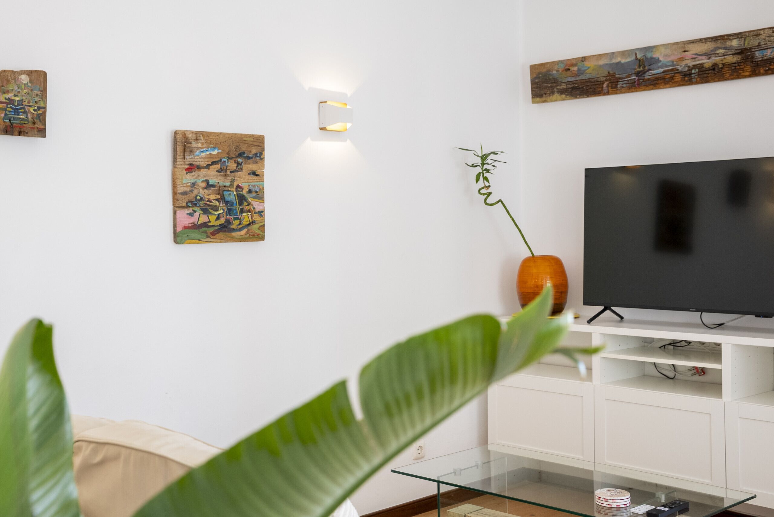 Ein Wohnzimmer mit einem Flachbildfernseher, weißen Schränken und Kunstwerken an den Wänden.