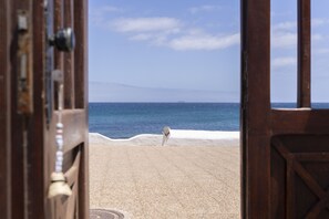 Blick durch eine Holztür auf einen Strand mit blauem Himmel und Meer.
