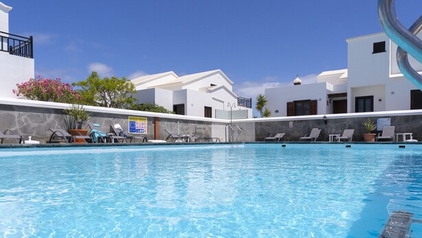 Una piscina con lettini, edifici bianchi e un cielo azzurro limpido.