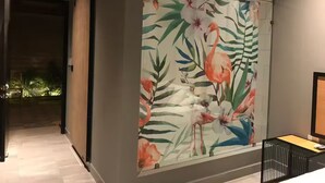 Une pièce décorée d’une grande œuvre d’art florale au mur, avec un lit doté d’une tête de lit noire et une petite table sur laquelle se trouve une lampe.