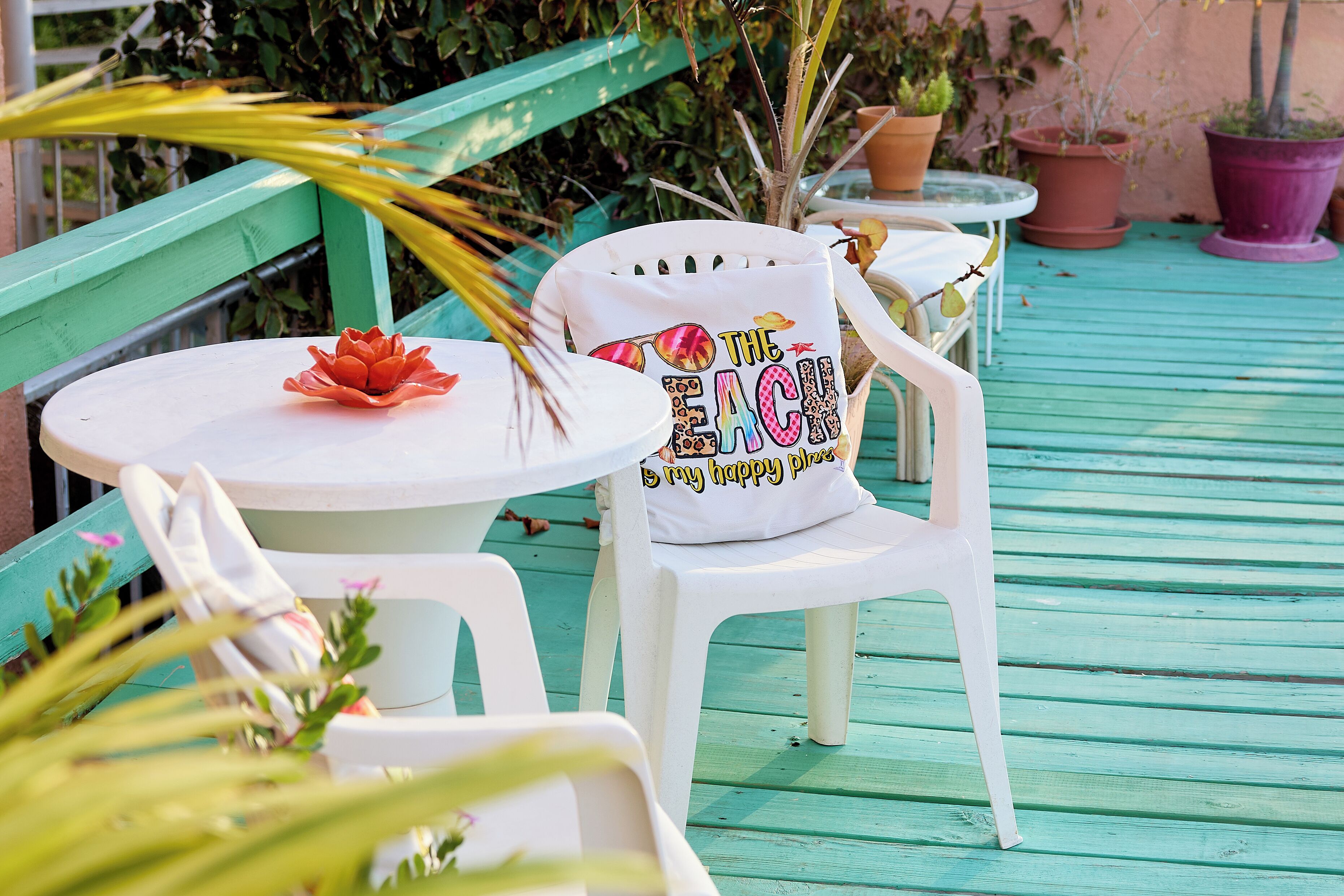 A patio area with a white plastic chair and table, a red flower in a white pot, and several potted plants.