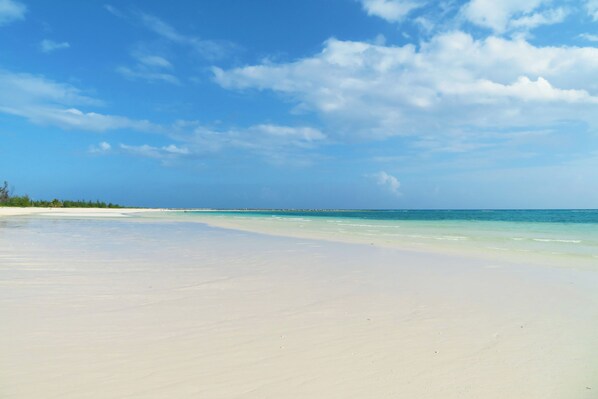 A beach with clear water, a sandy shore, and a distant horizon.