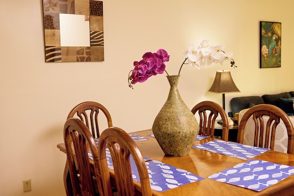 A dining table with a vase of flowers, wooden chairs, a lamp, and a wall with a mirror and artwork.