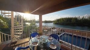A balcony with a table set for dining, overlooking a river and a pool.