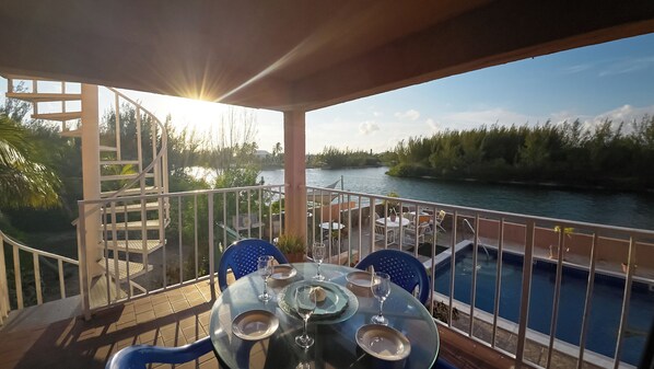 A balcony with a table set for dining, overlooking a river and a pool.