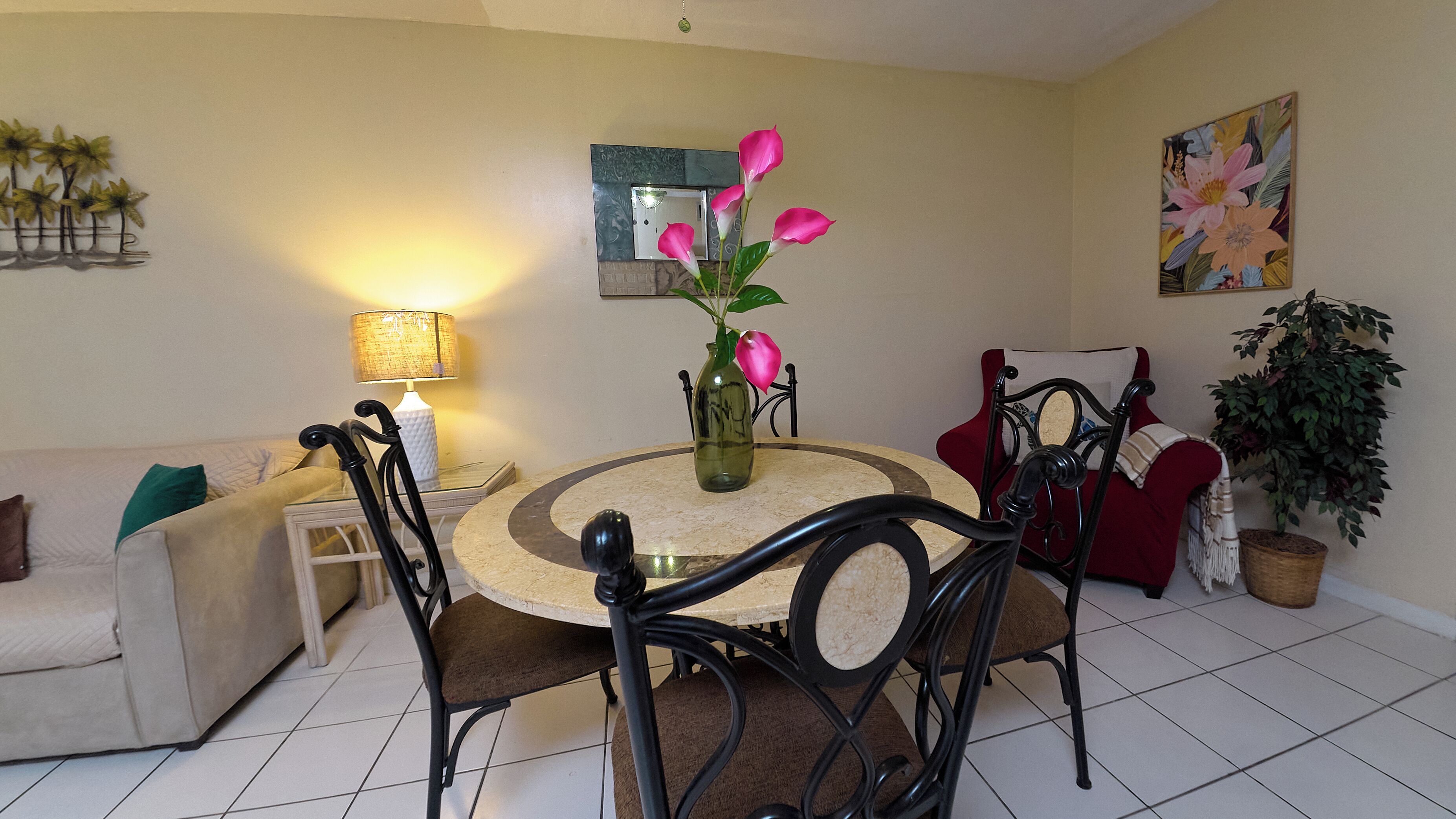 A dining area with a round table, chairs, a vase with flowers, a lamp, and a couch.