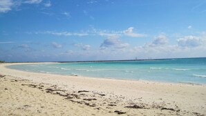 A beach with clear turquoise water, a sandy shore, and a distant horizon.