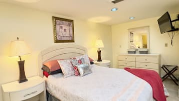 Un dormitorio con una cama, mesitas de noche, cómoda, televisor y una lámpara de techo.
