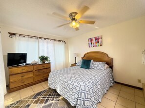 A bedroom with a bed, a TV, a dresser, a ceiling fan, and a window with curtains. - Dundee Bay Villas (Freeport)