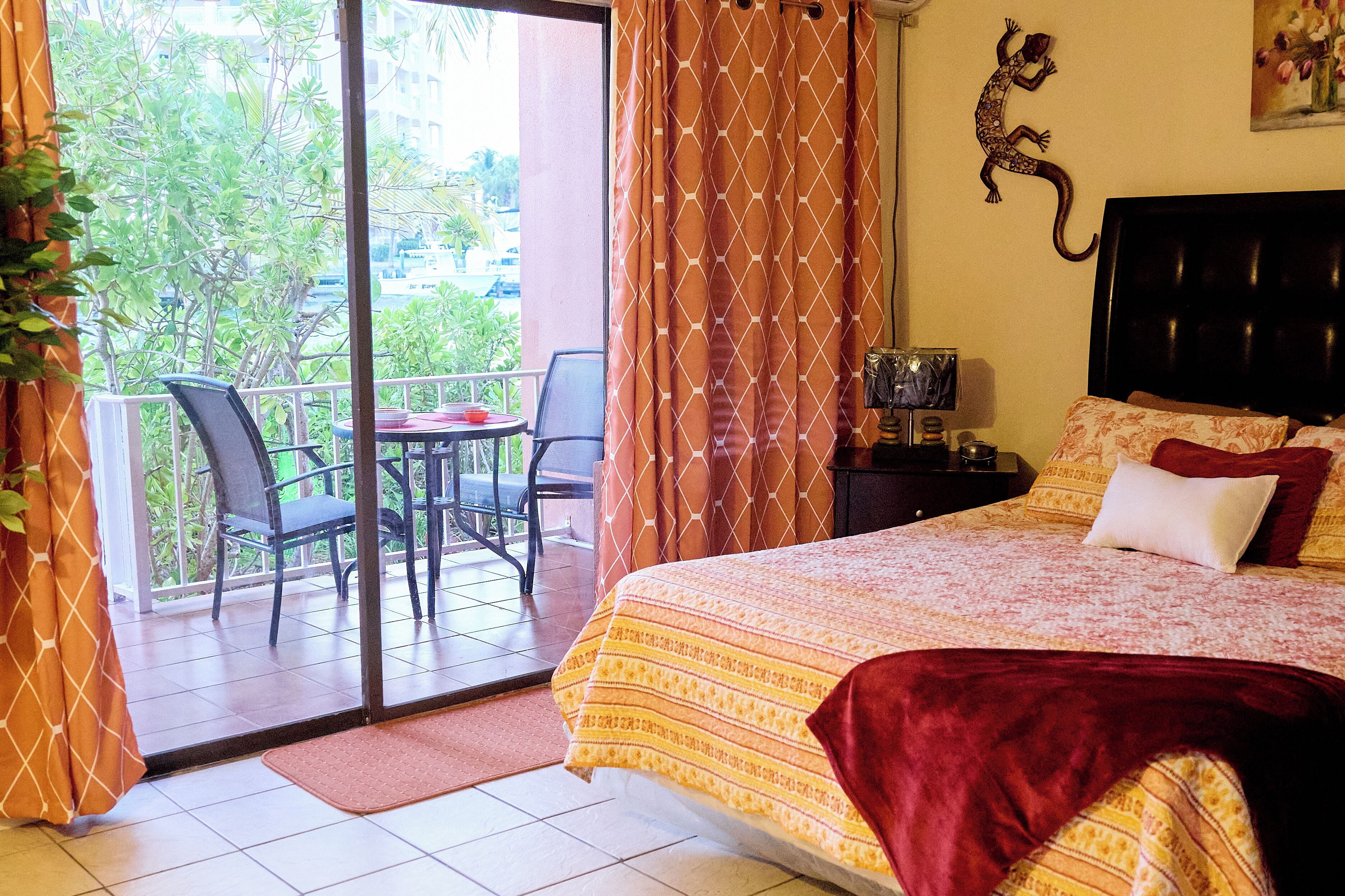 A hotel room with a bed, a desk, a chair, a window with curtains, and a view of greenery outside.