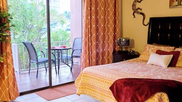 A hotel room with a bed, a desk, a chair, a window with curtains, and a view of greenery outside.