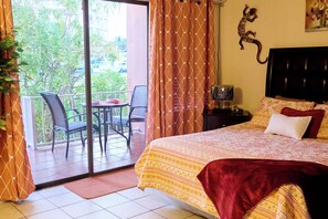 Een hotelkamer met een bed, een bureau, een stoel, een raam met gordijnen en uitzicht op groen.