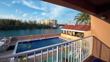 A pool area with a view of a body of water, a building with a red roof, and a palm tree.