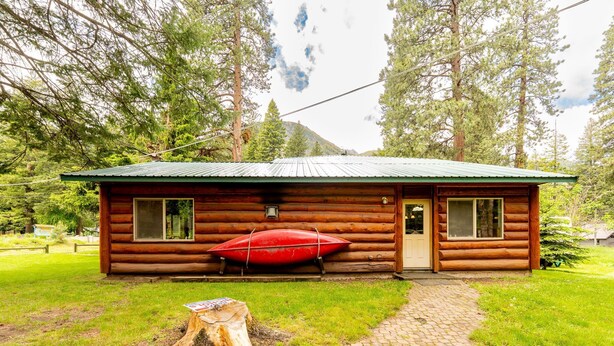 Una cabaña de troncos con techo verde, un canoa rojo y una terraza de madera.