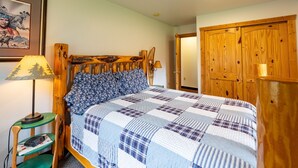 Un dormitorio con cabecera de madera, colcha acolchada, lámpara de noche y armario de madera.