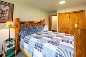 Een slaapkamer met een houten hoofdbord, een gewatteerde spreideken, een bedlamp en een houten kledingkast.