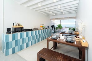 Una cocina moderna con un salpicadero azul y blanco a cuadros, una mesa de comedor de madera preparada para dos personas y vistas al mar desde el espacio abierto.