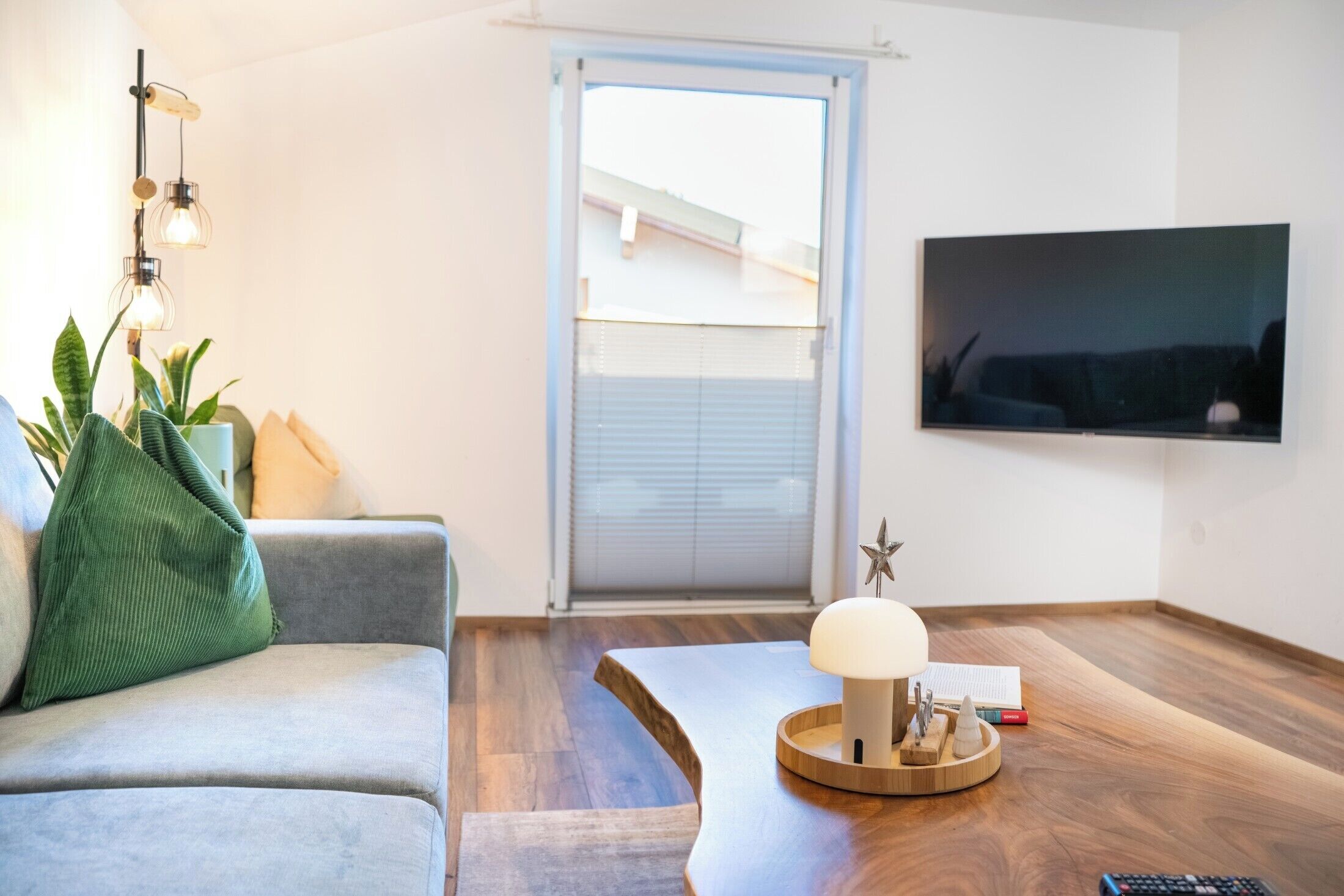 Ein Wohnzimmer mit einer Couch, einem Couchtisch, einem Fernseher und einem Fenster mit Jalousien.
