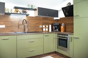 Eine Küche mit grünen Schränken, einer Holzrückwand, einer Kaffeemaschine und einem eingebauten Backofen.