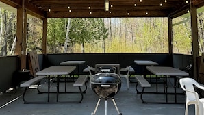 Un espacio al aire libre cubierto con una parrilla, mesas de picnic y bancos.