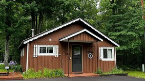 A small wooden cabin with a black door, white trim, and a circular emblem on the front.