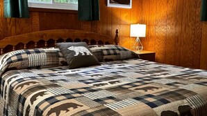 Una habitación con paneles de madera, una cama con colcha de cuadros y almohadas con motivos de animales.