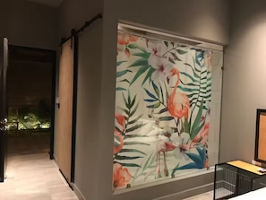 Ein Zimmer mit einem großen Blumenbild an der Wand, einem Bett mit schwarzem Kopfteil und einem kleinen Tisch mit einer Lampe.