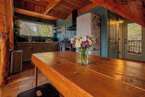 Ein Holzespeisekammer mit Blumen in einer Vase, eine Küche mit Holzschränken, einem Kühlschrank und einem Fenster mit Blick auf Bäume.