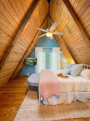 Ein gemütliches Schlafzimmer unter dem Dach mit einem Bett, einem Deckenventilator und einem an der Wand befestigten Fernseher.
