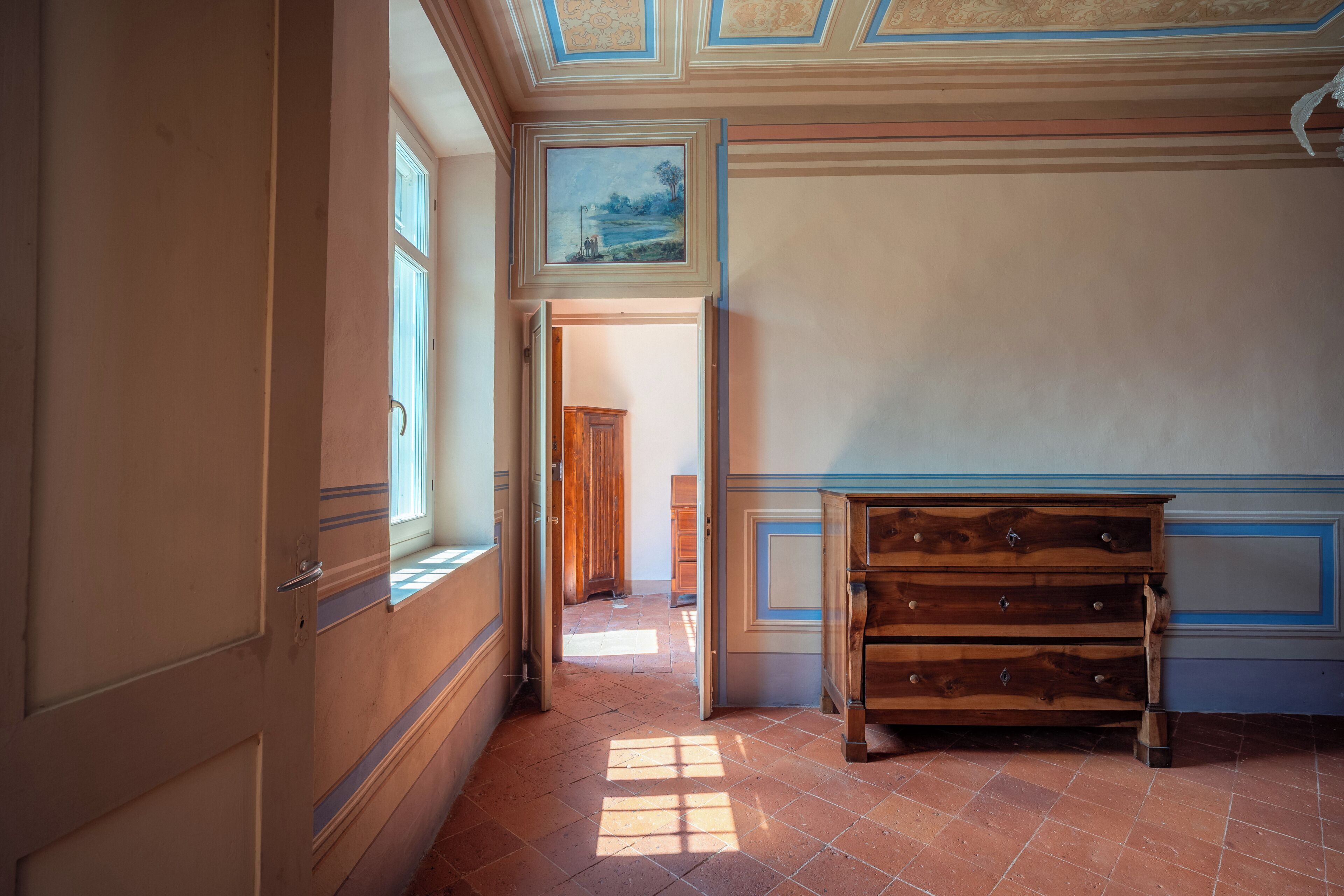Una habitación con un aparador de madera, un cuadro en la pared y una puerta que da a otra habitación.