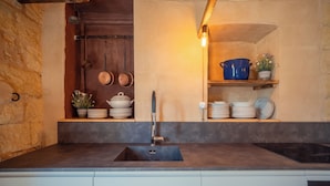Een keuken met een donker aanrecht, een spoelbak en planken met servies en pannen.