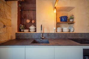 A kitchen with a dark countertop, a sink, and shelves with dishes and pots.