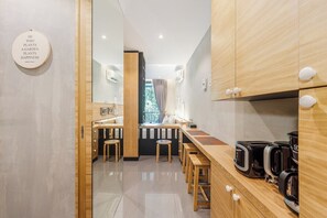 A modern kitchen with wooden cabinets, a coffee station, and a view through a glass door. - Woods Resort Kamala Pool • Gym • Near Beach C179 (กมลา)