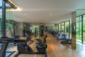 A gym with cardio machines, weightlifting equipment, and large windows offering a view of greenery. - Woods Resort Kamala Pool • Gym • Near Beach C179 (กมลา)