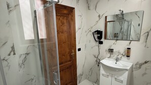 Et badeværelse med brusekabine i glas, en trädør, en marmorvæg, en vask med spejl og et toilet.